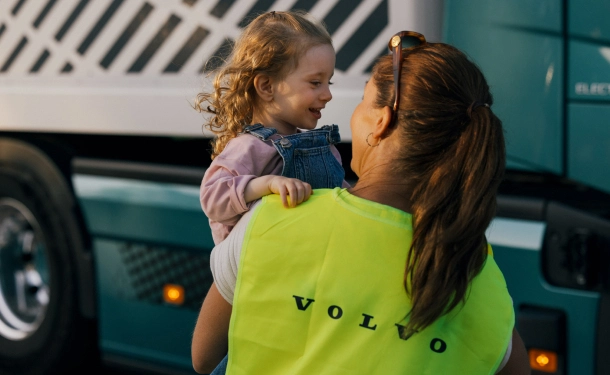 Volvo employee holding a young child in front of a truck.